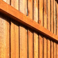 Close-up view of a wooden fence with vertical planks and a horizontal support beam, showing the warm brown color and texture of the wood in bright sunlight.